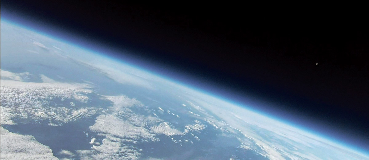 Pohled na planetu Zemi ze stratosféry. Nad zemským okrajem jsou vidět vrstvy stratosféry jako světle modré pruhy.  Vpravo je na temné obloze patrný i Měsíc. Autor: HVM a SOSA